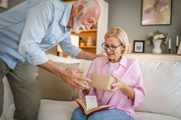 istock Senior husband surprised his mature wife whit gift while she read book 2162314044