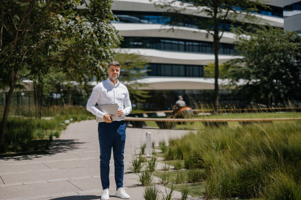 Man with laptop standing outside modern building, trees