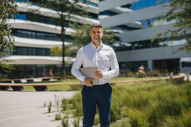 istock Man holding laptop outside, modern office, green park 2162314917