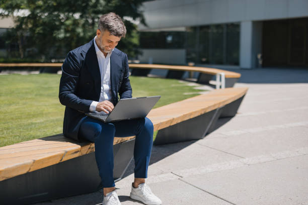 istock Man working on laptop while sitting on bench outdoors 2162314994