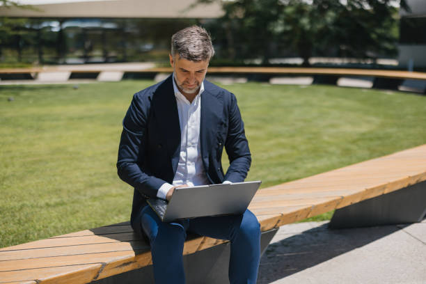 Businessman seated outdoors using laptop, green background