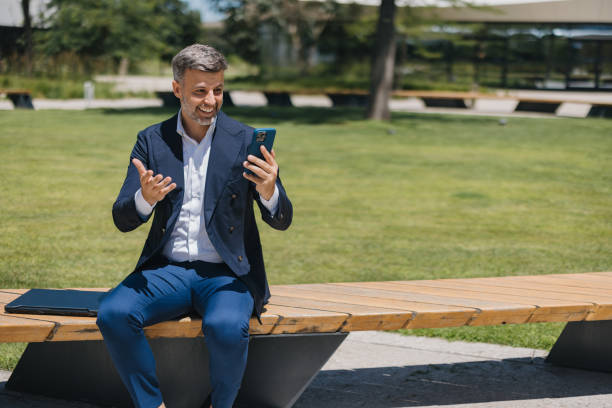 istock Man in suit having video call, seated outdoors on bench 2162315037