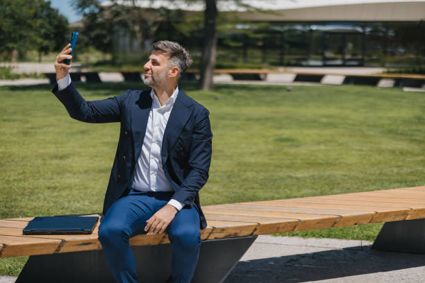 istock Man seated on a bench taking a selfie with a phone. 2162315049