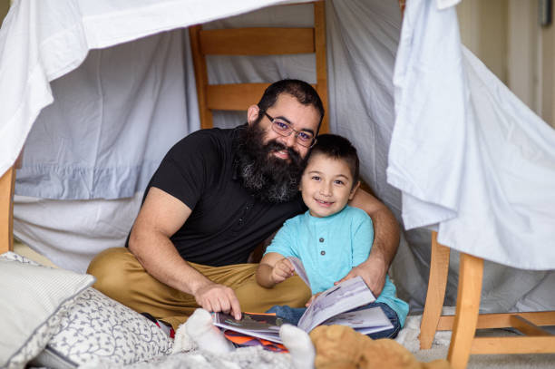 istock Father and son smile while reading book at home 2162319507