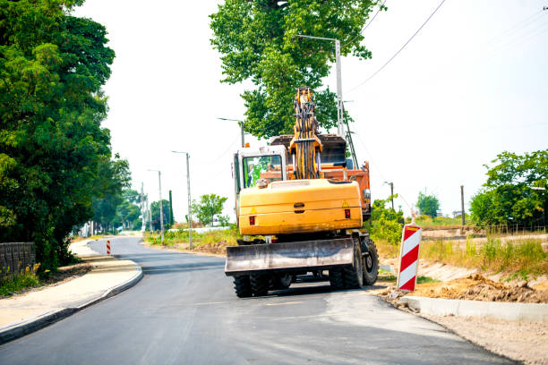Yellow construction machines on the road with an excavator. An excavator is a heavy construction machine designed for various tasks, including digging, lifting, and moving large objects. Widely used in construction, mining, landscaping, and other industries, excavators are essential for handling tough jobs efficiently and effectively.