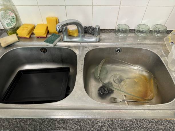 Stock photo showing close-up, elevated view of stainless steel, double kitchen sink full of dirty dishes.
* Not AI modified * imagen de fregaderos dobles de acero inoxidable con grifo mezclador de doble palanca montado en la plataforma, fregadero sucio lleno de platos sin lavar, esponjas de lavar amarillas antihigiénicas con estropajos verdes, líquido de lavado de botellas, fil