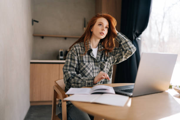 istock Low-angle view of thoughtful female student working or learning online on laptop looking away thinking of solution sitting at home desk using computer 2162328643