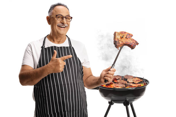 istock Mature man grilling meat on a barbecue and holding a steak on a fork 2162334672