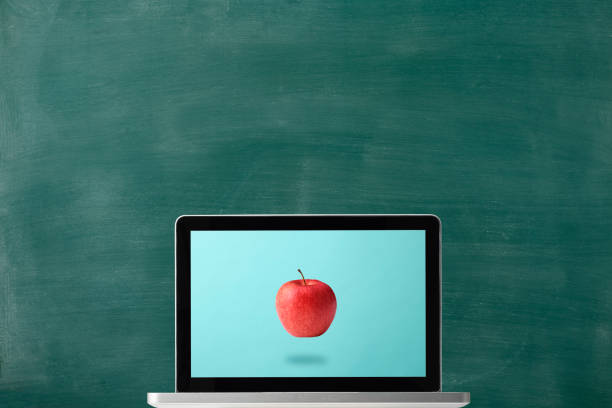 Red apple in mid-air displayed on a laptop in front of a chalkboard with copy space.\nBack to school concept.