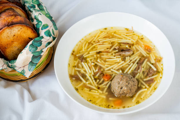 Beef broth soup with noodle, liver dumpling and cerrot soup in white plate, toasted fried bread in basket.