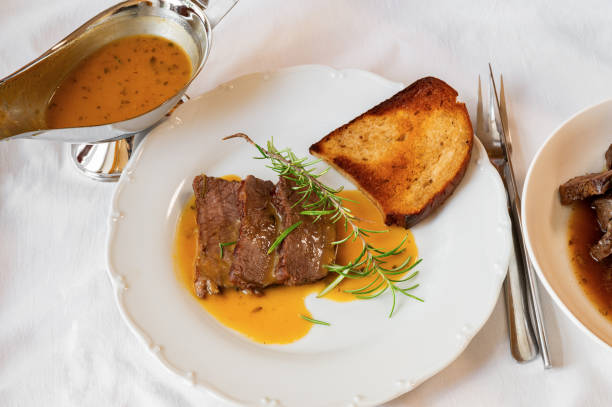 Baked venison loin with orange sauce, herb and fried bread on white.