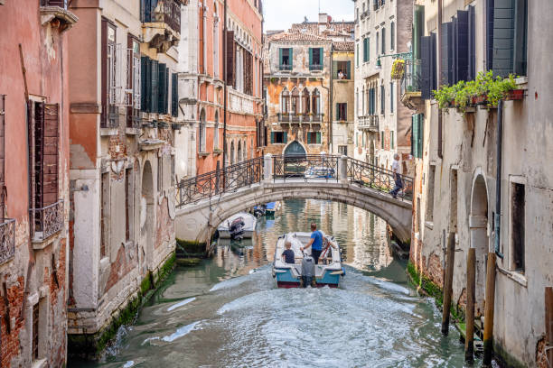 Venice, Italy - June 6th 2024:  Father and son sailing under a bridge in a motorboat in the center of Venice