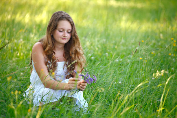 Young girl with long hair in white dress picking flowers on the meadow