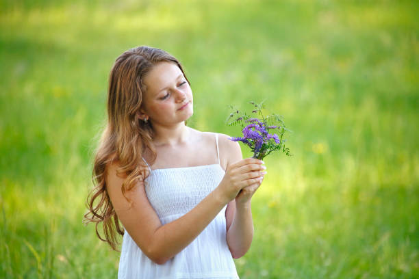 Young girl with long hair in white dress picking flowers on the meadow