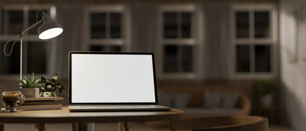 istock A laptop computer mockup, illuminated by light from a table lamp on a wooden table. 2162369115