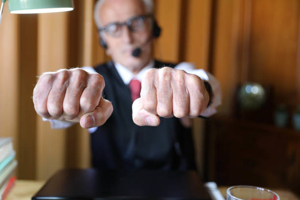 An elderly man in his office is showing a fist.