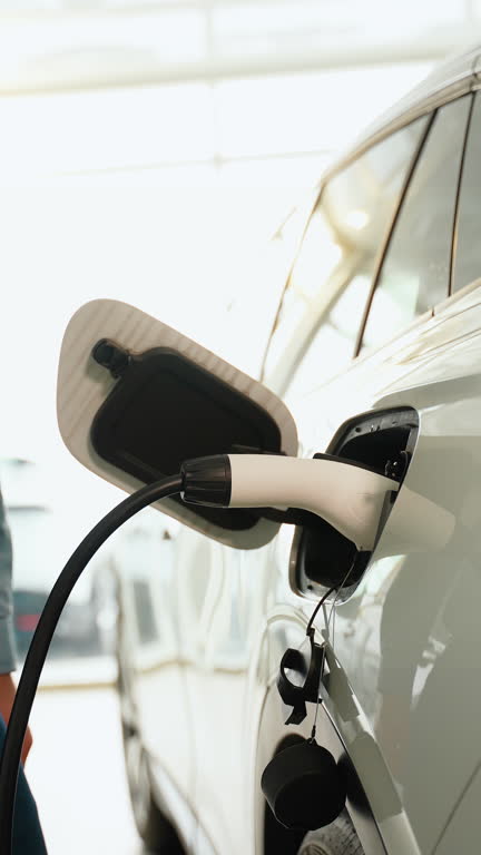 Close-up of man's hand, inserting a charger in luxury electric car in dealership. Vertical video