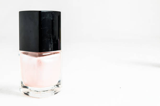 A bottle of nail polish sits on a white table. The bottle is clear and has a pink color