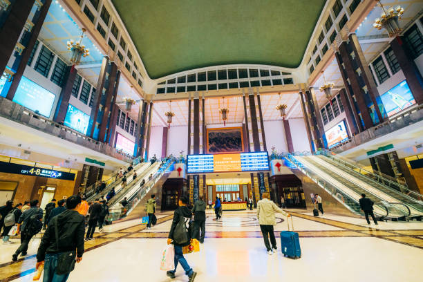 Busy scene of commuters at Beijing Railway Station on October 12, 2023. People are seen with luggage and walking towards escalators in entrance hall.
