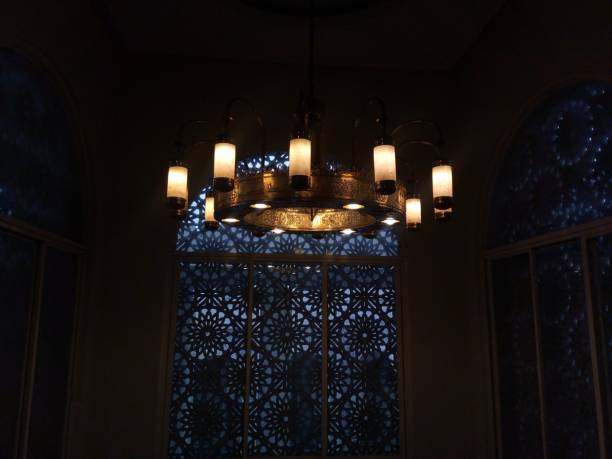 Ankara, Turkey – May 02,  2022 :Worshippers are seen praying inside the historical Aslanhane Mosque in Ankara, Turkey. The image captures the serene atmosphere of the mosque, with warm sunlight illuminating the ornate doors while the interior remains dimly lit, reflecting the spiritual essence of Islamic prayer rituals.