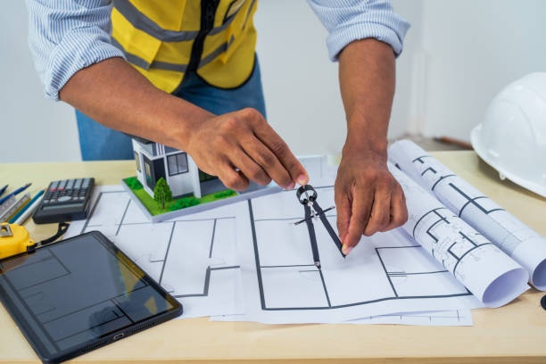 istock Asian architect works at a desk with house blueprints, checking plans on a laptop and clipboard, wearing a hardhat and safety vest, emphasizing precision and safety in office settings. 2162397227
