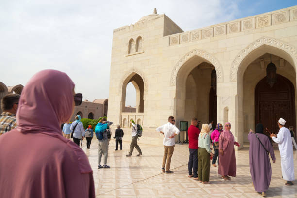 People, tourists in Inner courtyard covered walkway with columns in the Sultan Qaboos Grand Mosque with people in background.  Muscat Sultanate of Oman
