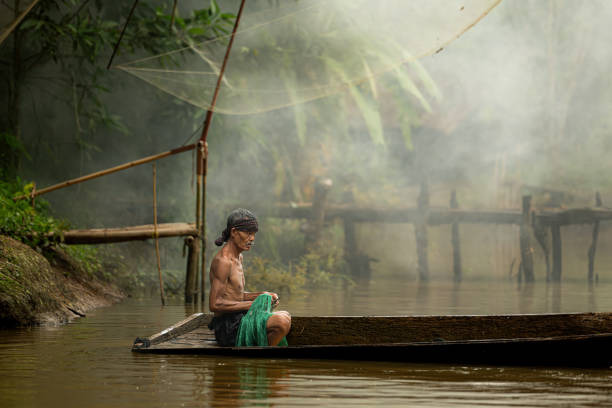 istock Fisherman on a boat in the river using a fishnet to catch fish 2162402595