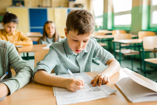 istock portrait of elementary schoolboy writing in workbook at desk in classroom 2162418464