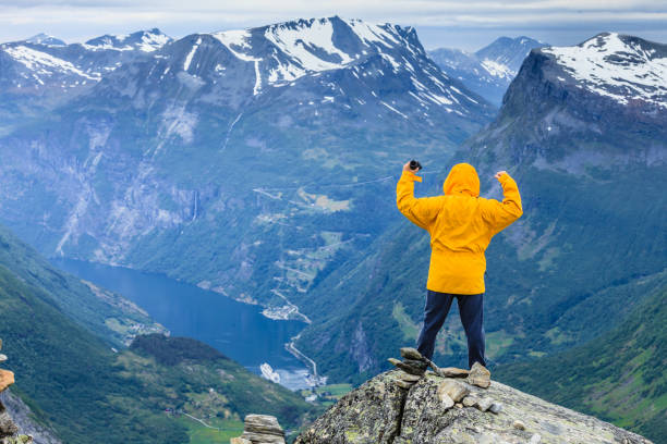 Tourism vacation and travel. Male tourist taking photo with camera, enjoying Geiranger fjord and mountains landscape from Dalsnibba Plateau viewpoint, Norway Scandinavia.