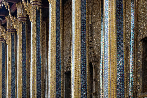 The image showcases a temple in Thailand, resplendent in gold and blue patterns. The side view reveals the temple's slender columns, dark backdrop.