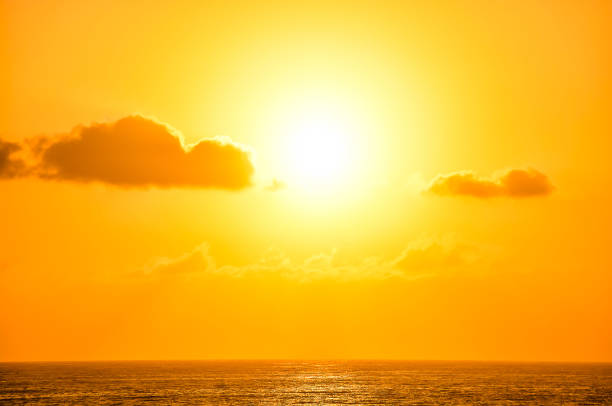 The sun is setting over the ocean, casting a warm glow over the water. The sky is filled with clouds, creating a serene and peaceful atmosphere