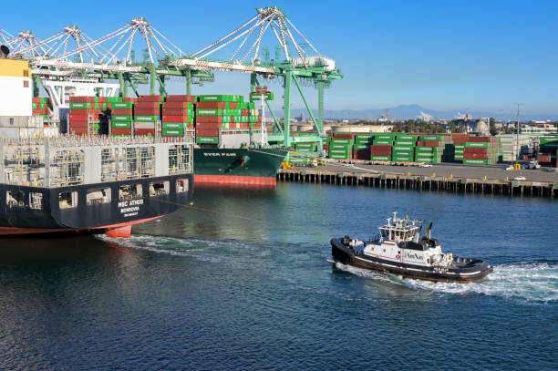 San Pedro, Los Angeles, California, USA - November 12, 2024: Sunset light shines on a tug boat helping a liquefied natural gas ship through the port of Los Angeles.