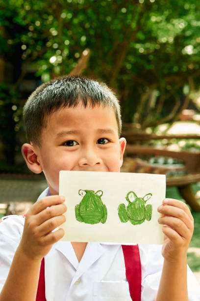 Close-up of small schoolboy showing frog drawing while standing outside in schoolyard