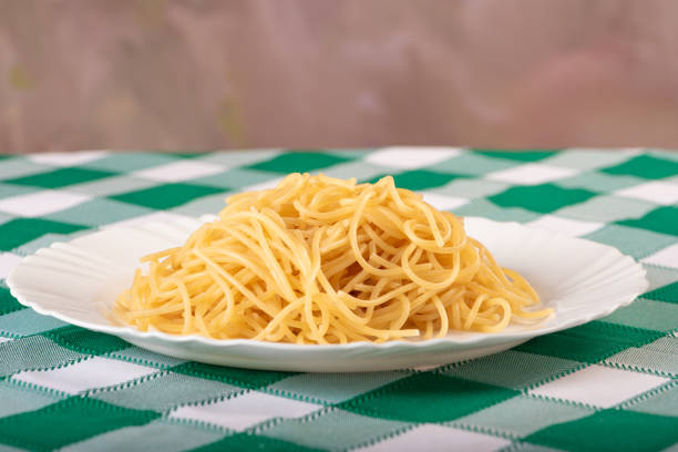 Pasta, spaghetti noodles on a white plate, on a green and white checkered tablecloth. Selective focus.