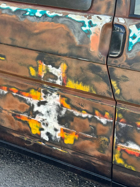 Stock photo showing close-up view of a rusted car door that has had graffiti spray paint sanded down to leave multicoloured patches of paint.