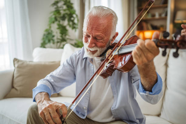 senior man learn to play violin at home online teacher teach or have private online class on tablet whit mature woman in the background