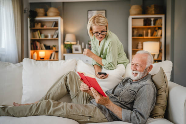 istock Senior husband lying down on sofa and read book whit his mature wife 2162454499