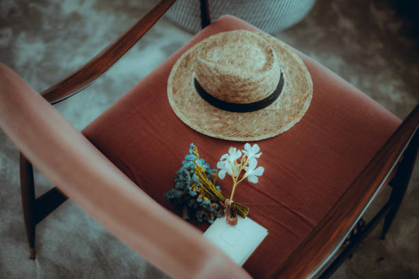 A close-up view of a straw hat, a small bouquet of dried flowers, and a white notecard placed on a red upholstered chair. The scene is cozy and well-lit, with a shallow depth of field