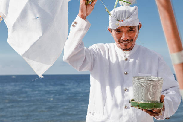 Balinese man smiling and waving his hand while holding blank paper on a clipboard
