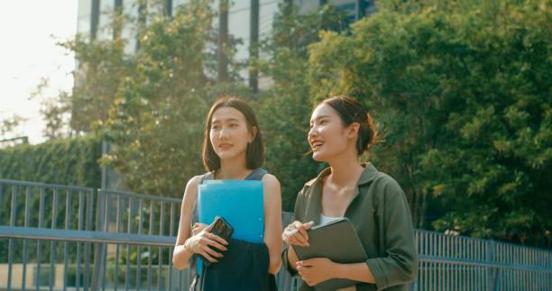 istock Two young Asian businesswomen discussing work while holds digital tablet and carries documents while walking outside office building. Sustainable business outdoor. 2162495390
