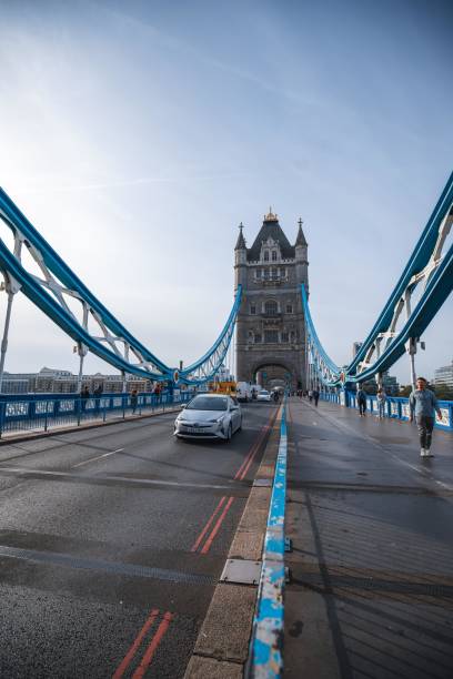 A view of Tower Bridge in London, UK, with a car driving over the bridge and pedestrians walking on the sidewalk. London, UK - October 09, 2023 : A view of Tower Bridge in London, UK, with a car driving over the bridge and pedestrians walking on the sidewalk. dorchester on thames stock pictures, royalty-free photos & images