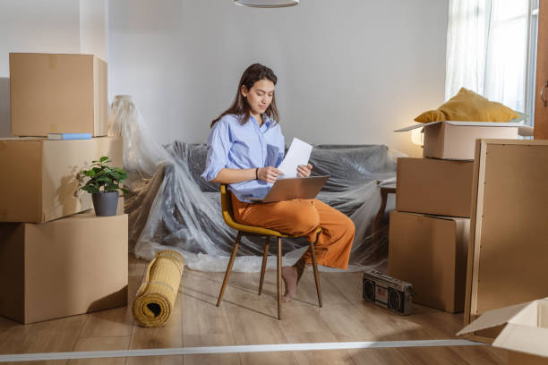 istock Young woman using laptop in new home and holding documents 2162498892
