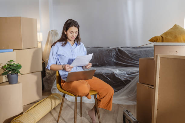 istock Young woman using laptop in new home and holding documents 2162499767