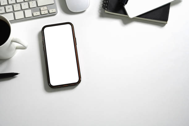 istock Smartphone with empty screen, coffee cup and stationery on white office desk. Top view 2162503379