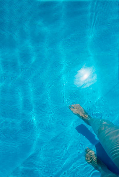 Woman Stepping into a swimming pool blue water on sunny Summer day. Female legs walk underwater. Copy space. Vertical image
