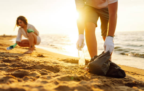 Cleanup garbage on the ocean coast. Cleanup garbage on the ocean coast. Volunteers with polyethielene bag picking up a plastic bottle on the beach. The concept of conservation of ecology. Earth day. earth day clean up stock pictures, royalty-free photos & images