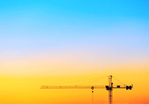 Crane is silhouetted against a beautiful orange sky. Crane machinery at construction site