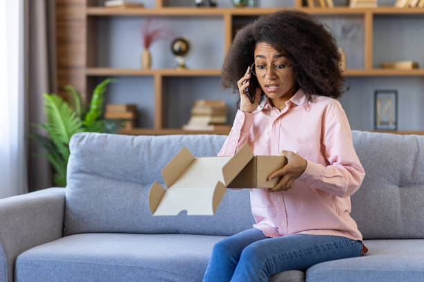 istock Worried woman on phone discovering empty package while sitting on sofa at home 2162513333