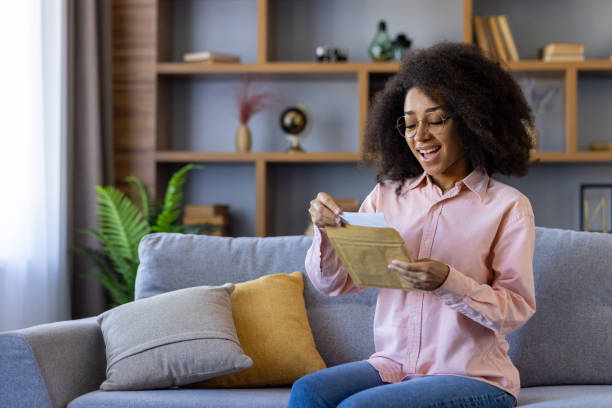 Happy woman opening envelope on cozy sofa at home