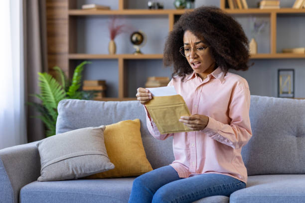 istock Woman sitting on sofa feeling surprised while reading a letter 2162513342